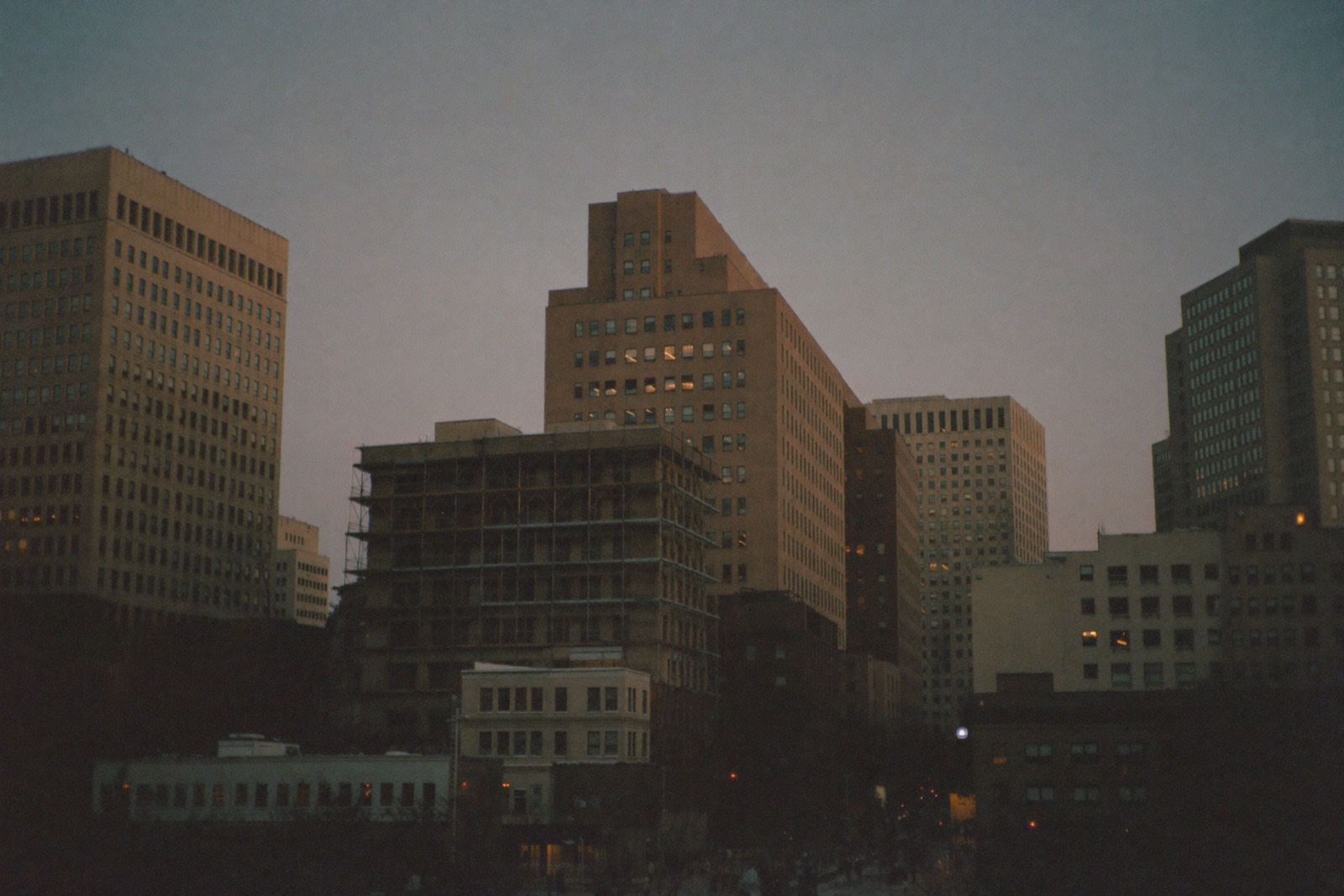 Downtown office towers at blue hour, one wrapped in construction scaffolding